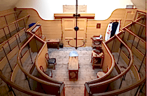 Photograph of the old operating theatre from the back. Bloodied aprons hang on the right-hand side.